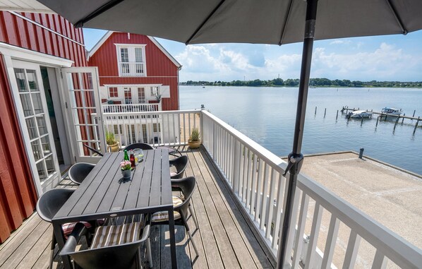 Een houten terras met een tafel en stoelen, met uitzicht op een rustig meer met bootjes.