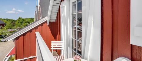 Un edificio rojo y blanco con un balcón blanco, una ventana y una planta en maceta.