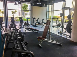 A gym with various exercise equipment, large windows, and a view of buildings outside.