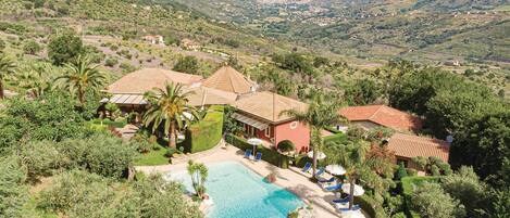 A resort with a swimming pool, palm trees, and a view of the surrounding hills.