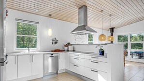 Eine moderne Küche mit weißen Schränken, einem Edelstahl-Geschirrspüler, einem großen Fenster und Blick ins Freie.