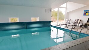 An indoor swimming pool with clear blue water, a tiled edge, and a few lounge chairs.