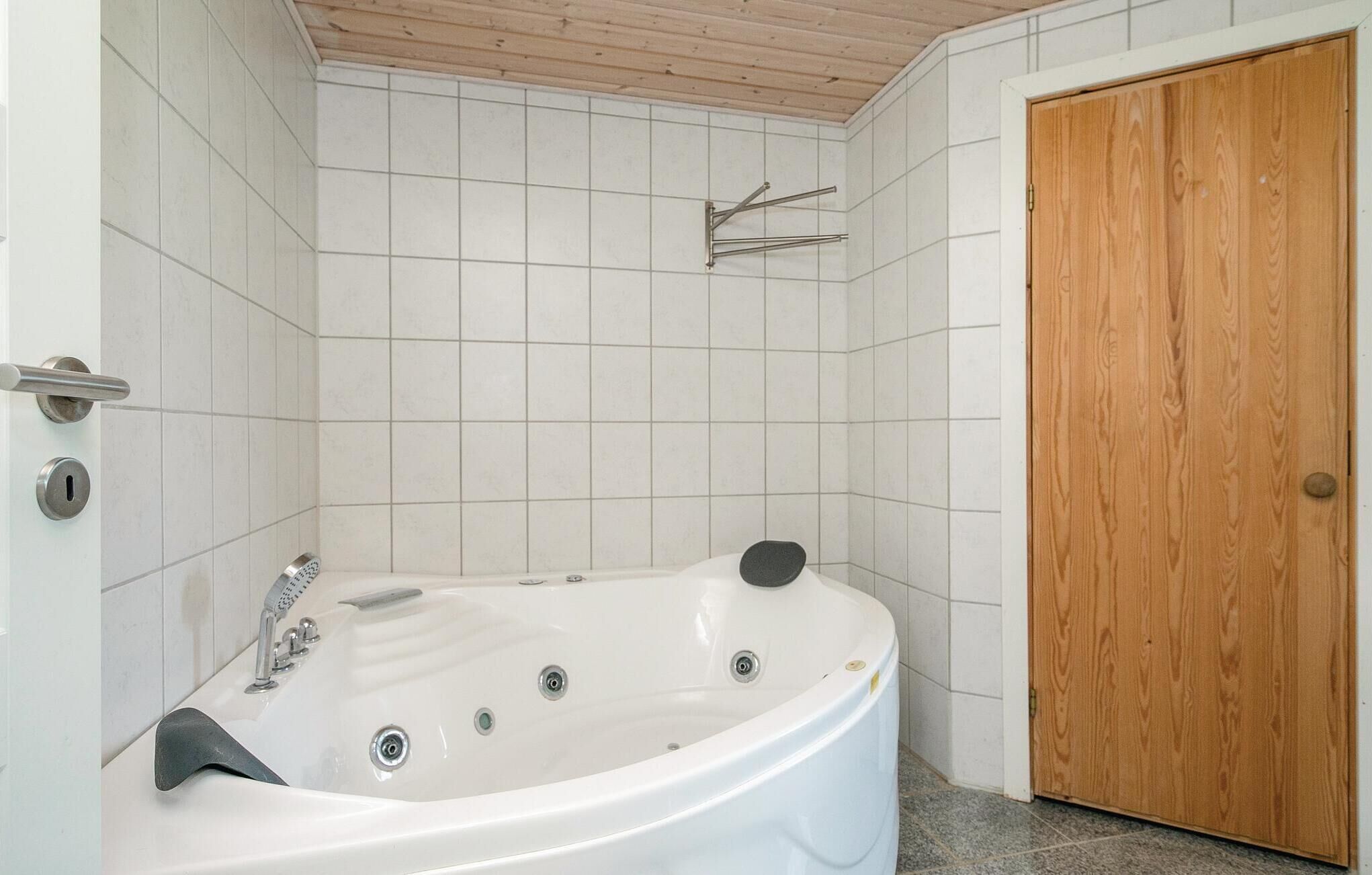 A bathroom with a white bathtub, a wooden door, and tiled walls.