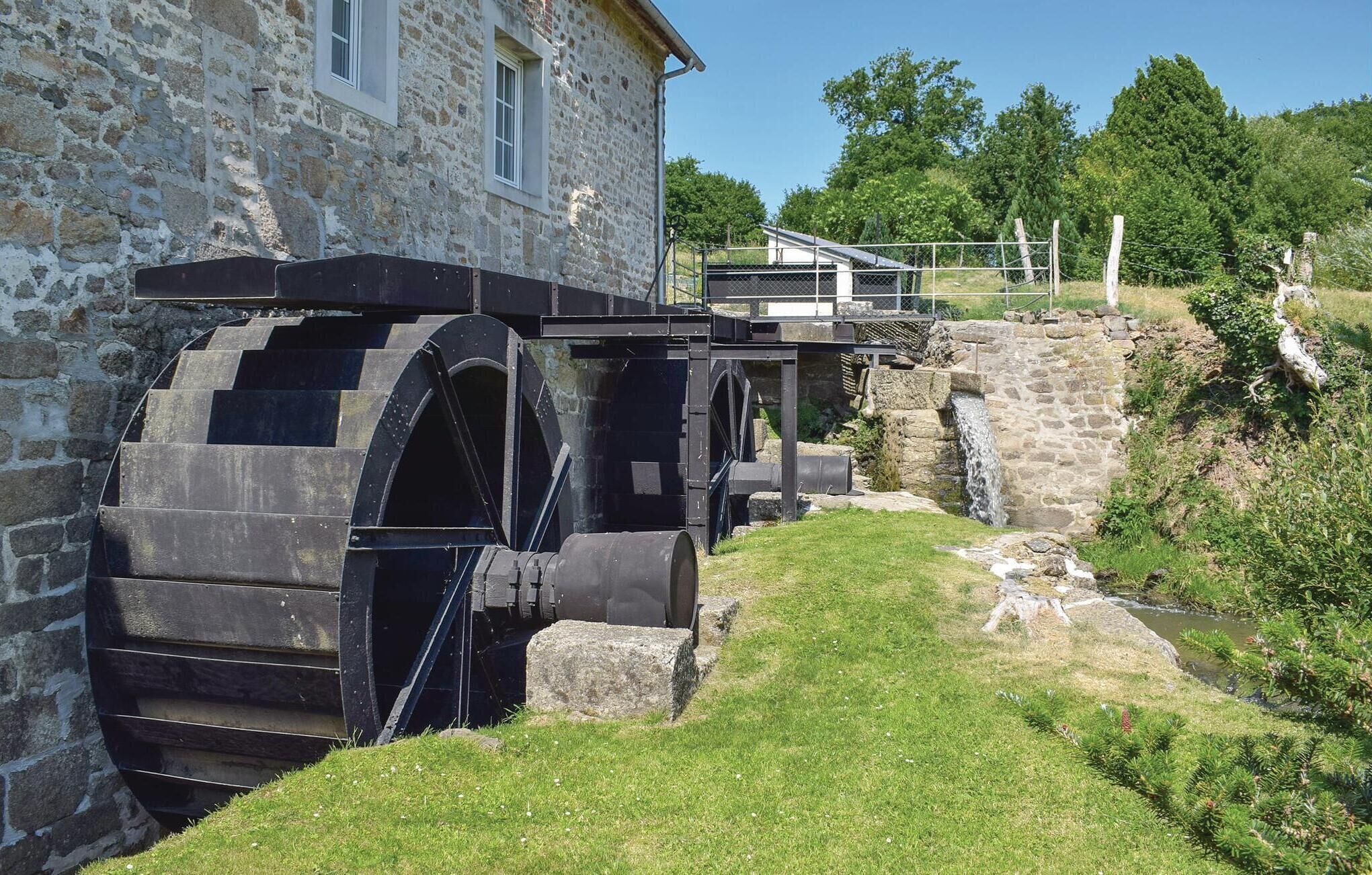 A historic stone building with a large water wheel and a small house on a hill.