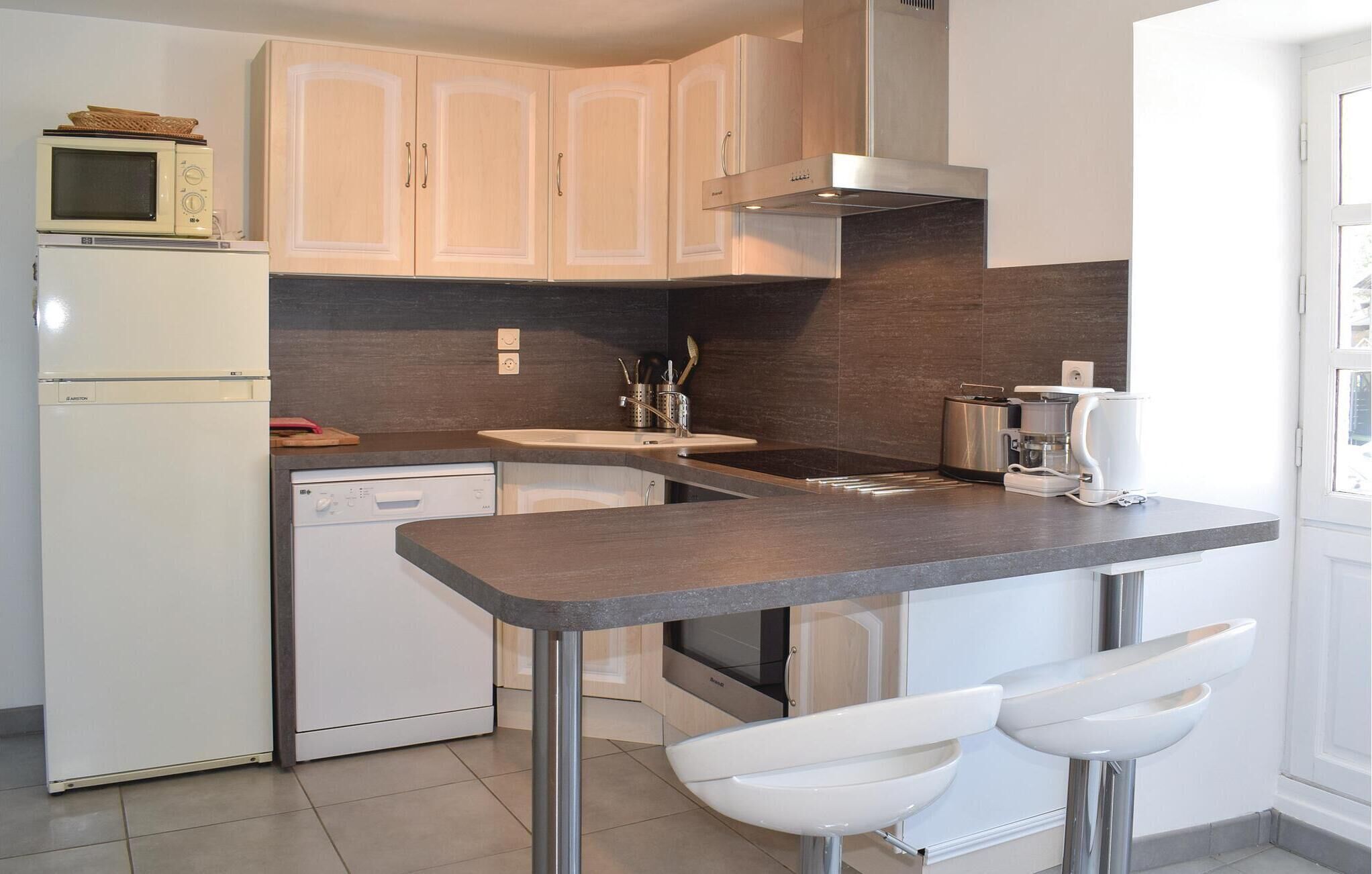 A compact kitchen with a built-in microwave, a dishwasher, a stove, and a coffee maker. There are two white bar stools and a small countertop.