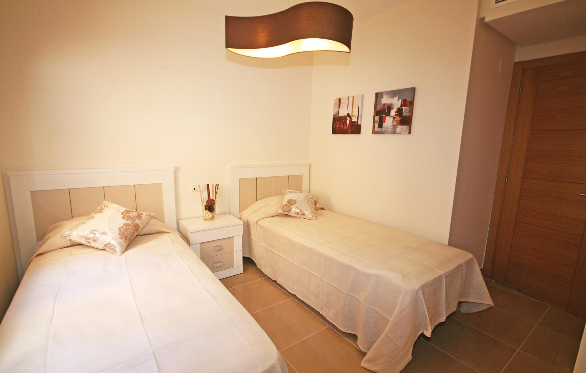 Un dormitorio con dos camas individuales, una mesita de noche con lámpara y un armario de madera.