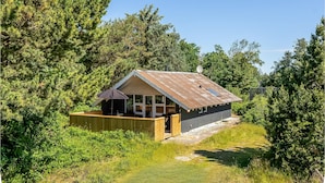 Une petite cabane dotée d’une terrasse en bois, entourée d’une forêt dense.