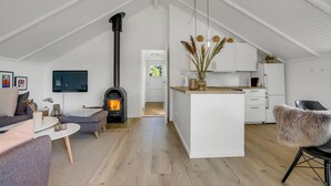 Un loft moderne doté d’un haut plafond, d’une cheminée centrale, d’une cuisine avec des meubles blancs et d’un coin salon confortable avec un canapé et une table basse.