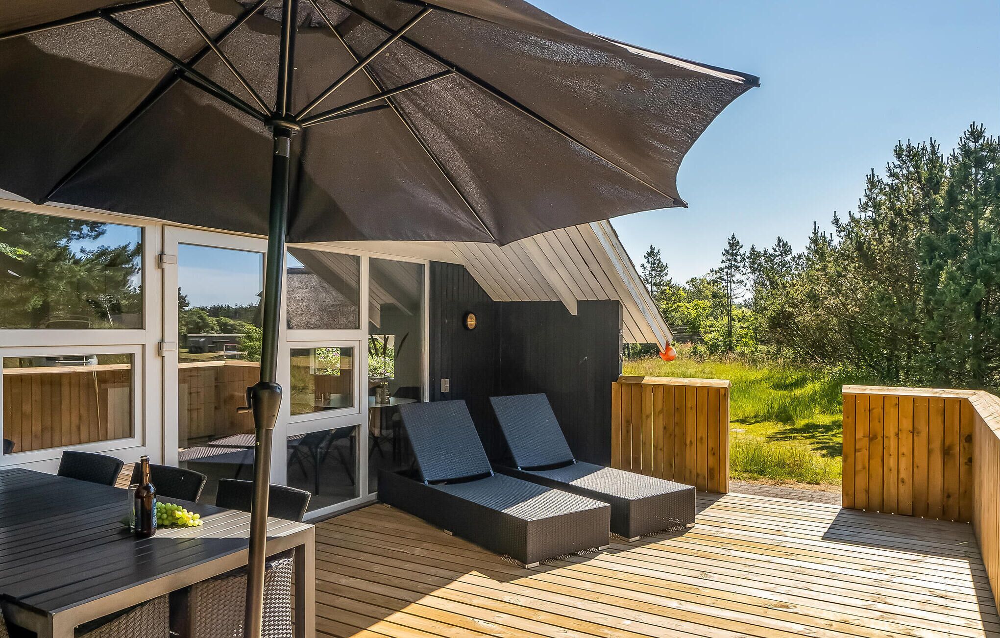 Eine Terrasse im Freien mit Tisch, Stühlen, einem großen Sonnenschirm und zwei Liegestühlen.