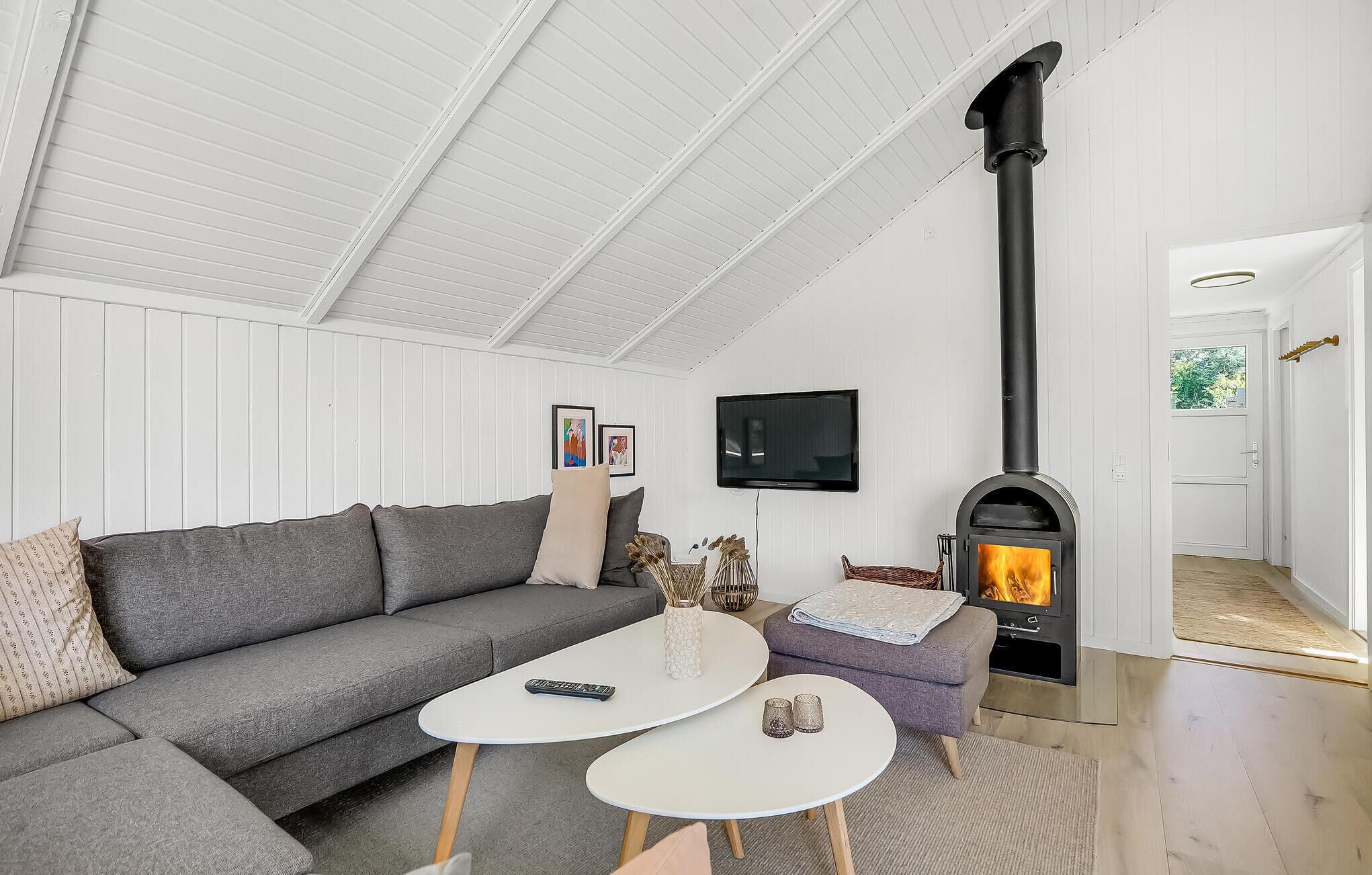 A modern living room with a grey sofa, two white coffee tables, a fireplace, and a television mounted on the wall.