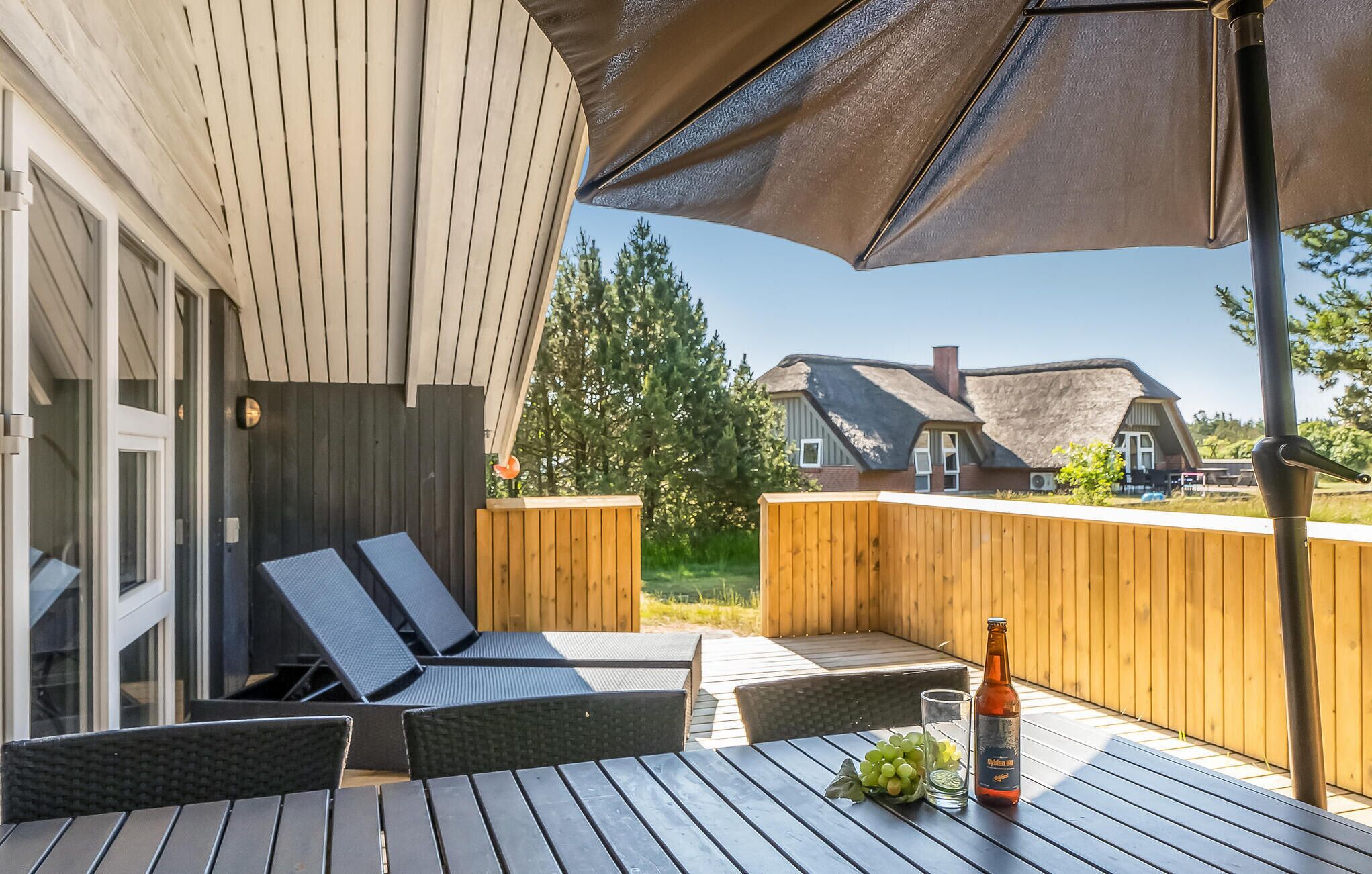 Une terrasse extérieure avec des meubles en bois, une bouteille de bière et un verre.