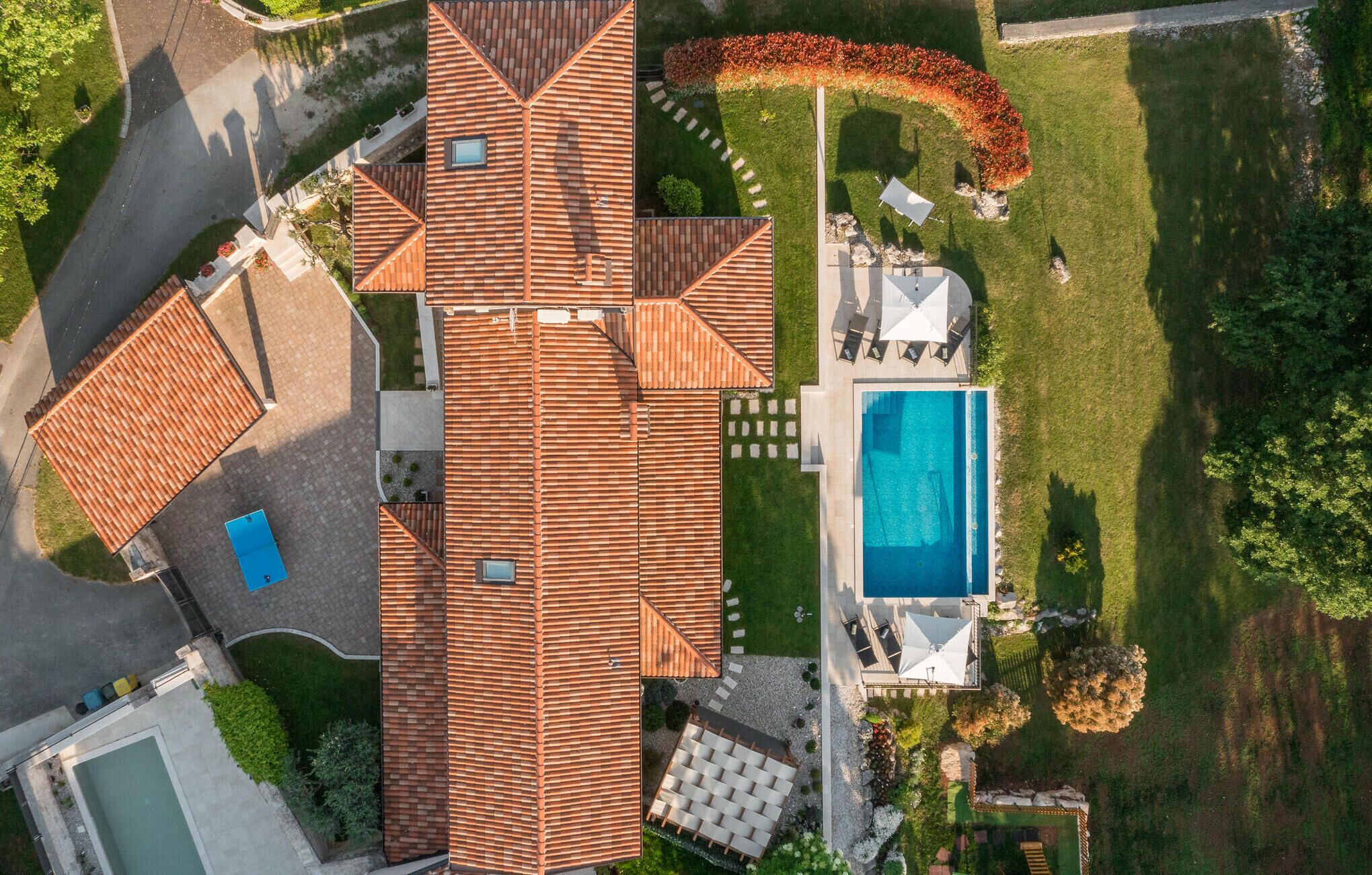 A residential property with a large tiled roof, a swimming pool, and a well-maintained garden.