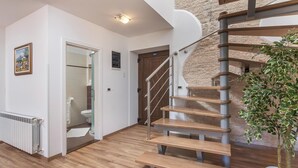 A modern interior with a wooden floor, a spiral staircase, and a view of a stone wall.