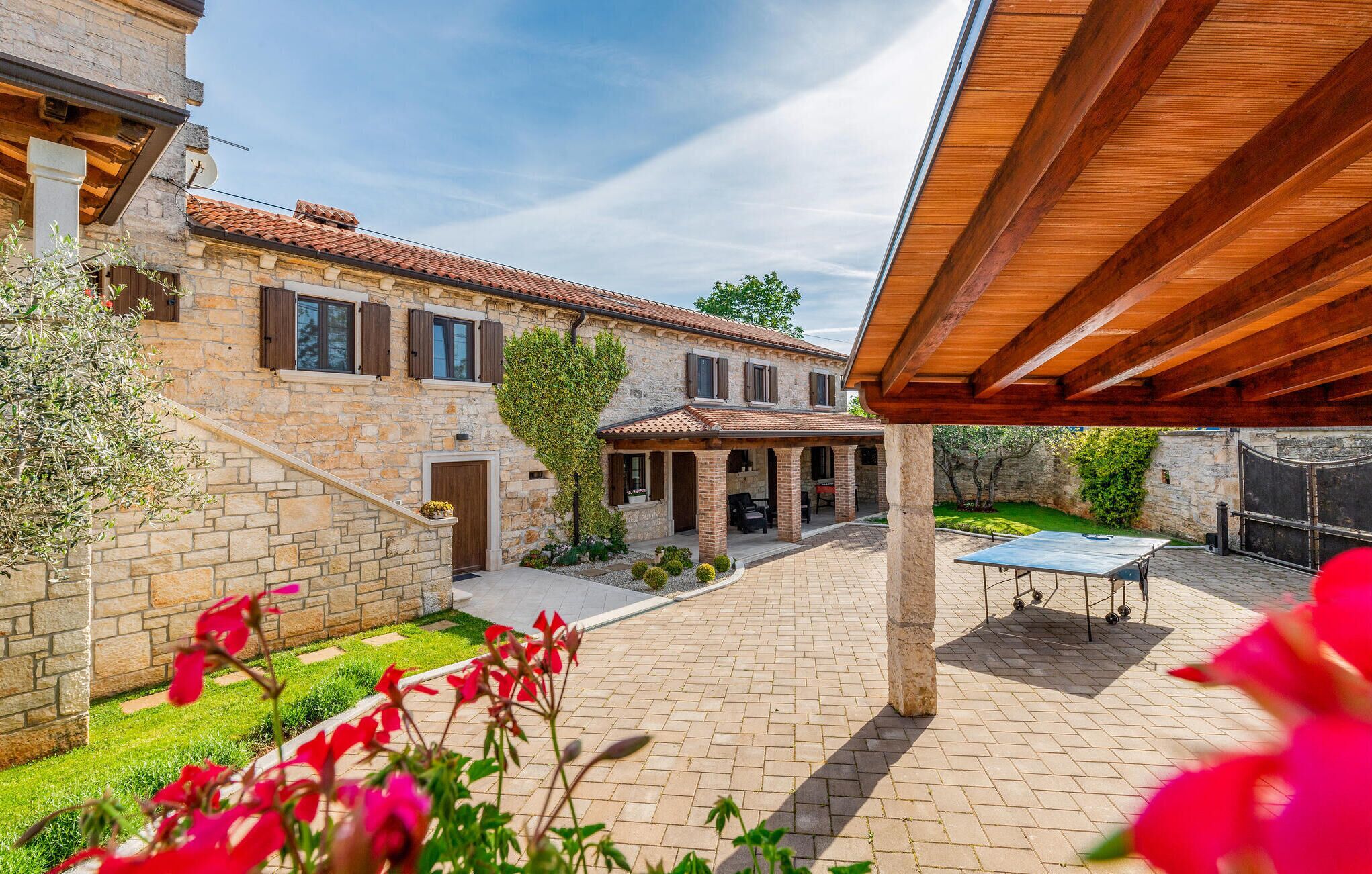 A stone house with a tiled roof, a covered patio area, and a ping pong table.