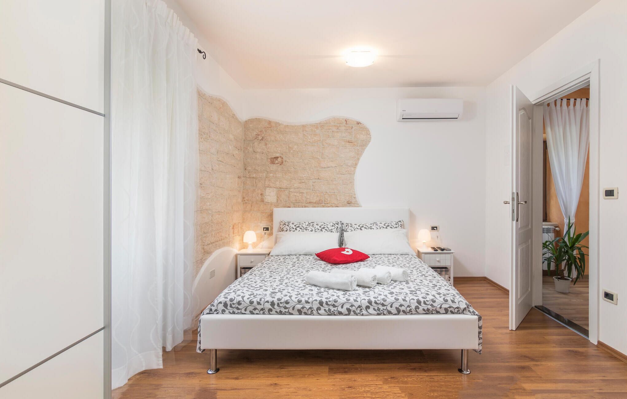 Een moderne slaapkamer met een bed, nachtkastjes, een wandairconditioner en een houten vloer.