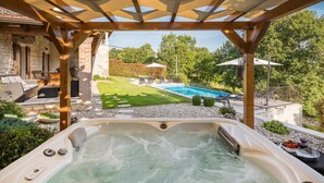 A hot tub in a backyard with a pool, stone walls, and outdoor furniture.