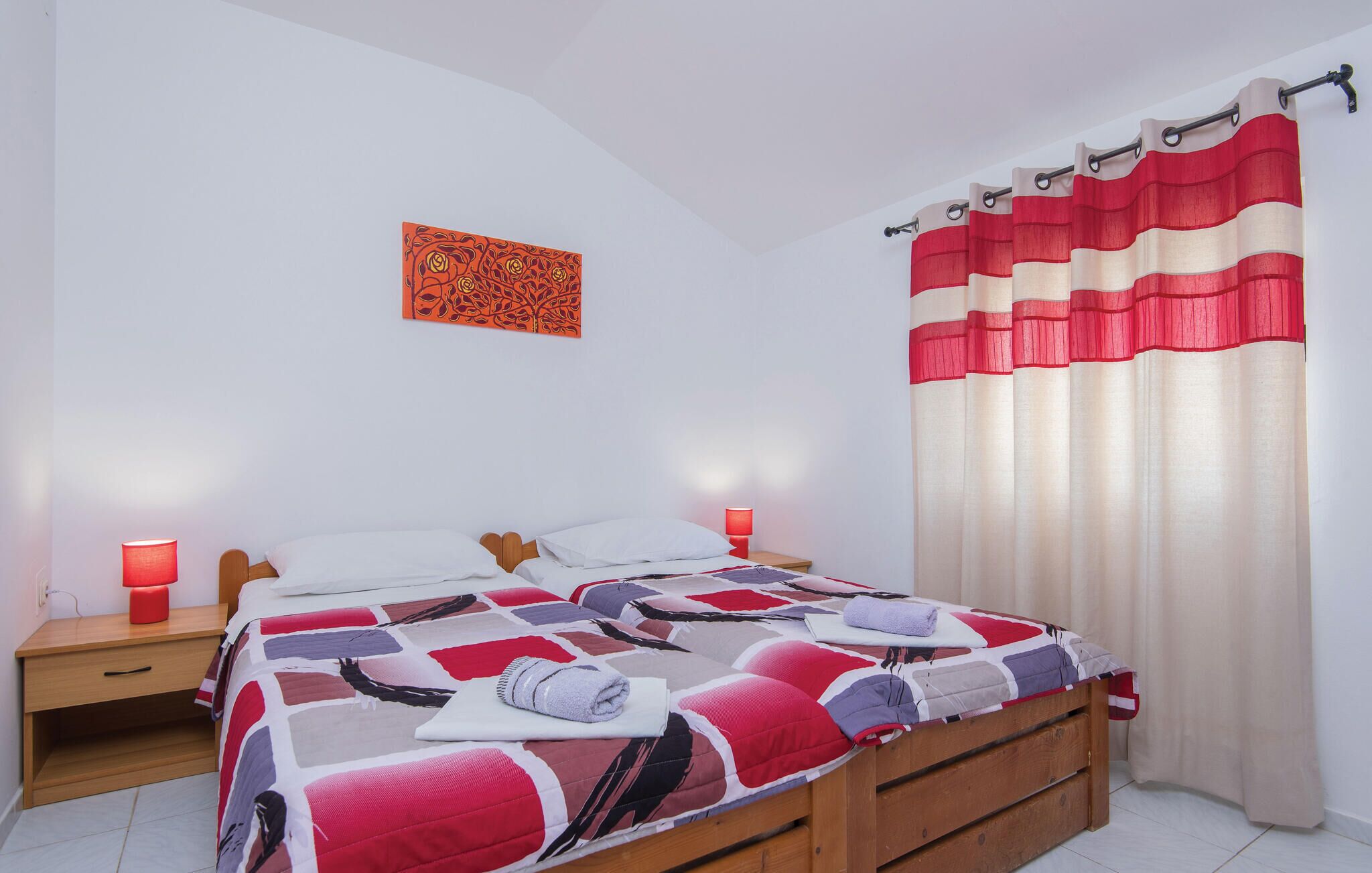 Un dormitorio con una cama de madera, una mesita de noche con una lámpara roja y una obra de arte colgada en la pared.