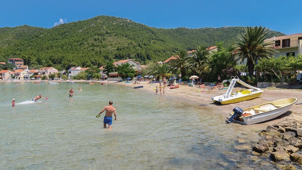 A beach with clear water, people swimming, and boats.