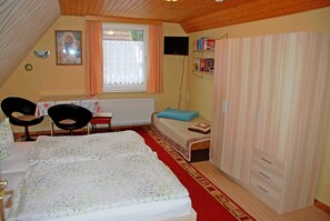 Une chambre à coucher comprenant un lit, deux chaises, une petite table, une fenêtre avec des rideaux, un radiateur, un téléviseur et une armoire.