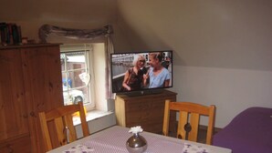 A small room with a wooden table, a television on a wooden cabinet, and a window with a view of the outside. - 2 - - - floor 3 room (BC. A3) - BARLT - Ferienhaus Bärbel (Barlt)