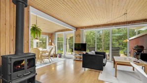 A modern living room with a wood-burning stove, large windows, and a cozy seating area. - Pet friendly home in Hadsund with sauna (Hadsund)