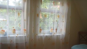 Ein Schlafzimmer mit Bett, einem Fenster mit durchsichtigen Vorhängen und Blick ins Grüne.