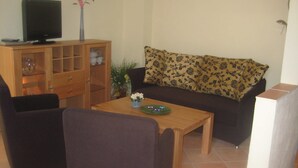 Ein Wohnzimmer mit einer Couch, zwei Sesseln, einem Couchtisch, einem Fernseher auf einem Schrank und einer Vitrine.