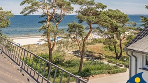 A coastal view with pine trees, a beach, and a building with a balcony. - Villa Strandperle, Whg. 33 // - VS 33 (Heringsdorf)