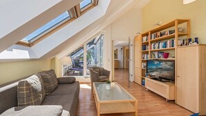 A modern loft apartment with a sloped ceiling, a sofa, a coffee table, a bookshelf, and a television. - Villa Strandperle, Whg. 33 // - VS 33 (Heringsdorf)