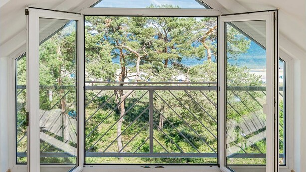 A room with a large sliding glass door leading to a balcony with a view of trees and a body of water. - Villa Strandperle, Whg. 33 // - VS 33 (Heringsdorf)