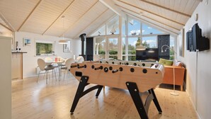 Un acogedor loft con techo de madera, una mesa de fútbol de mesa, un televisor y un ventanal con vistas a zonas verdes.