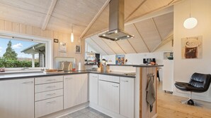 Una cocina moderna con armarios blancos, una isla central y un amplio ventanal con vistas a zonas verdes.