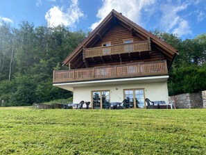 A two-story wooden chalet with a balcony, large windows, and a stone wall. - Double room (apartment 1) - log cabin (Sangerhausen)