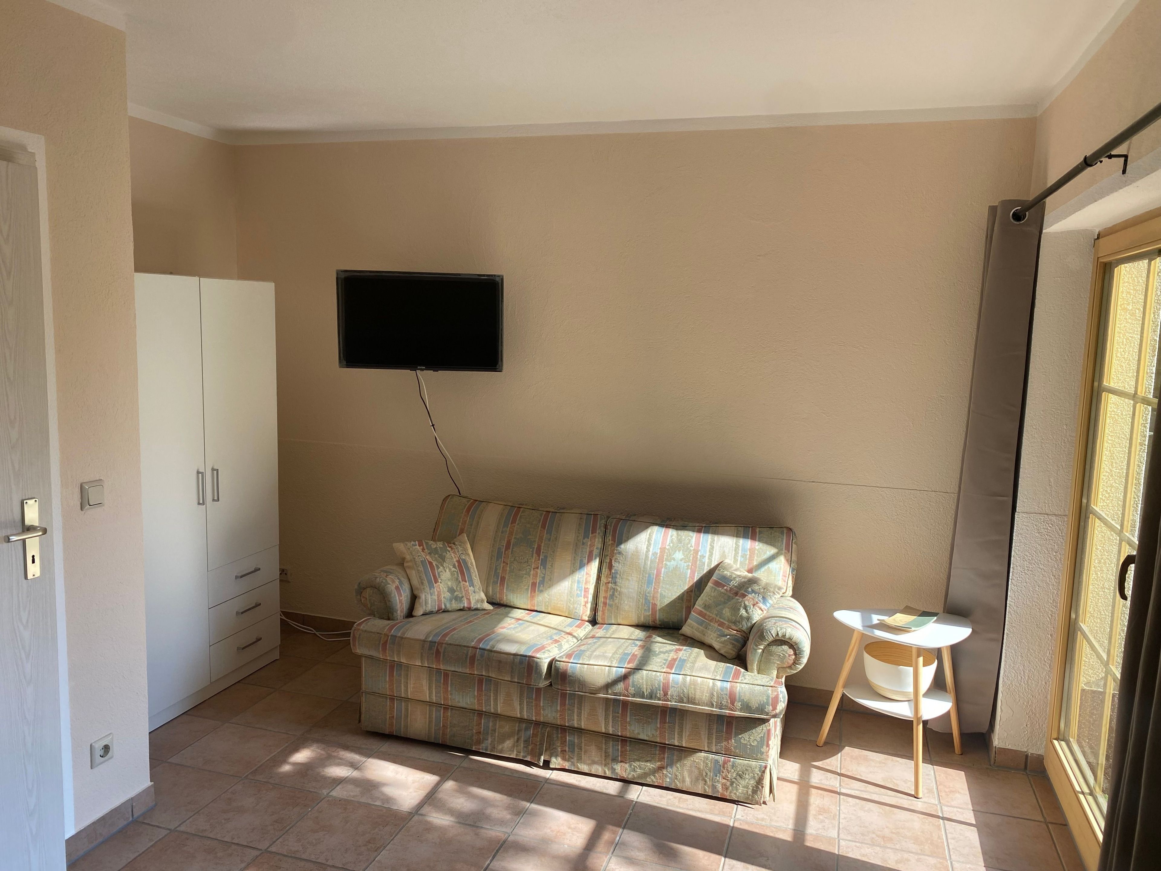 Una habitación con sofá, televisor en la pared, una mesita y una puerta.