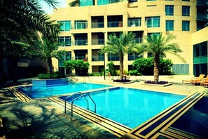 A swimming pool surrounded by palm trees and a multi-story building with balconies. - Piks Key - Burj Views B (Dubai)