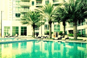 A swimming pool with lounge chairs and palm trees in front of a modern building.