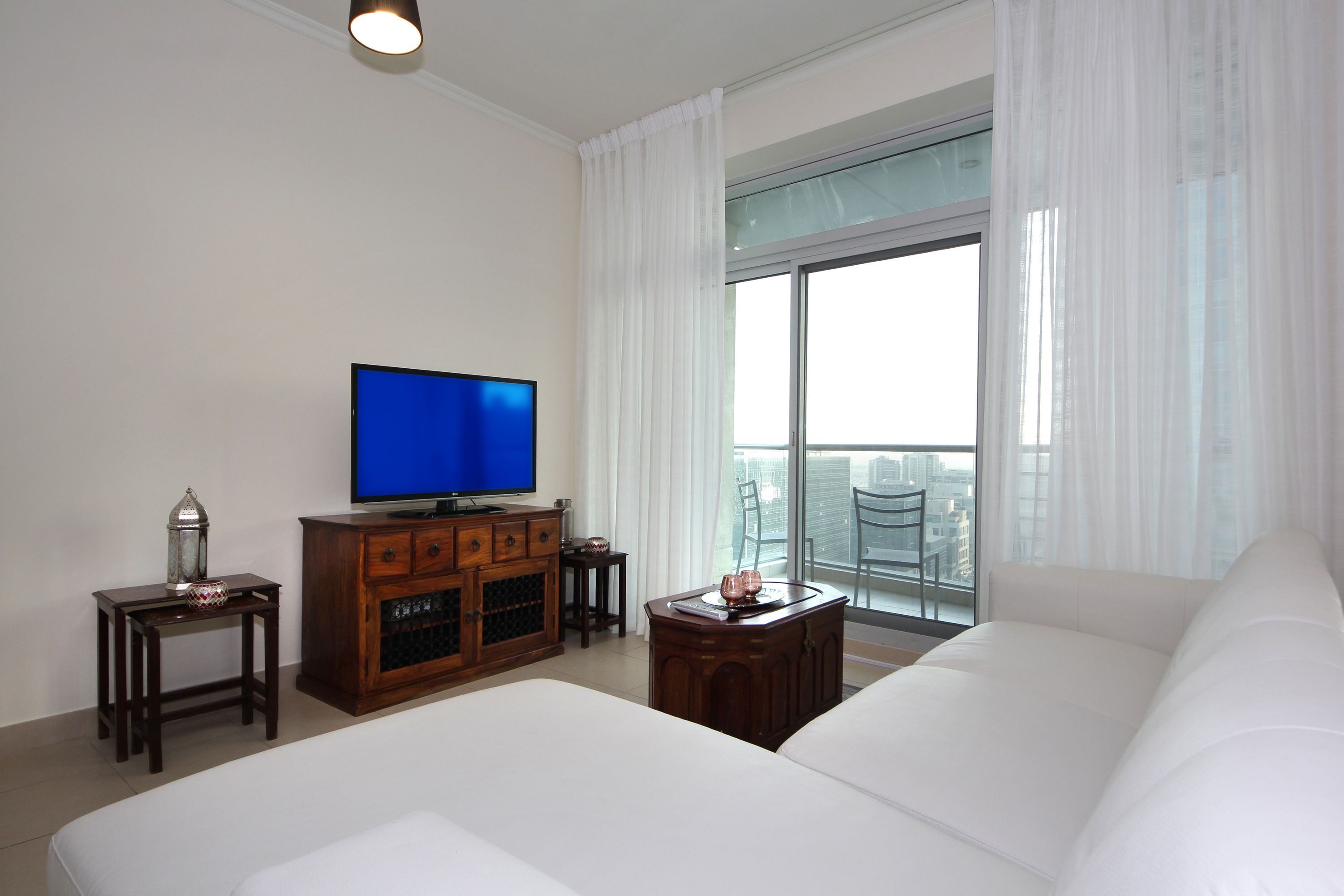 Een hotelkamer met een groot bed, een televisie, een houten kast en een balkon met uitzicht op de stad.