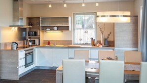 A modern kitchen with built-in appliances, a dining area with chairs, and a large window providing natural light. - Holiday home Strandmuschel - FH Strandmuschel (Loddin)