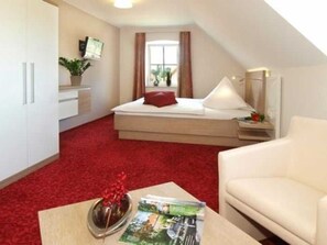 A compact hotel room with a bed, a small desk, a chair, a TV, and a window with curtains.