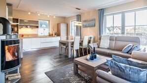 A modern living room with a fireplace, a dining area, and a sofa with cushions. - Holiday home Strandmuschel - FH Strandmuschel (Loddin)