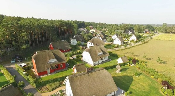 Maaseudun kylä, jossa on perinteisiä olkikattoisia taloja, ja kylää ympäröivät vihreät pellot ja tiheät metsät.