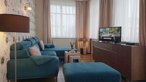 Een kamer met een bank, een poef, een televisie en een kleine tafel met een lamp.