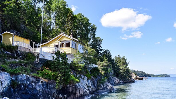 A yellow house with a white balcony, located on a rocky cliff by a calm body of water. - 3 bedroom awesome home in Nordre Frogn (Nordre Frogn)