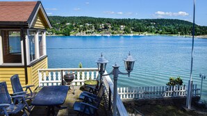 Eine Terrassenausstattung am Seeufer mit Sitzgelegenheiten im Freien, einem Grill und Blick auf einen See und bewaldete Hügel.