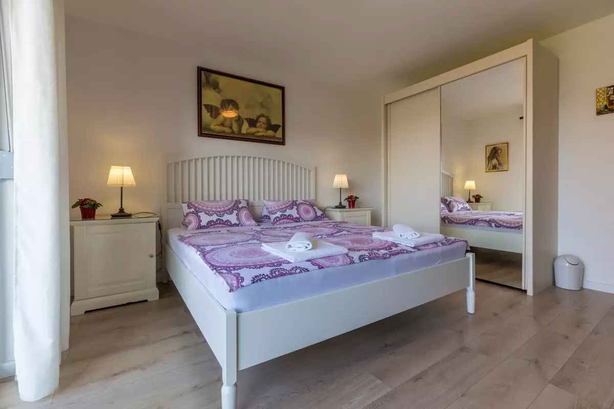 A bedroom with a bed, two bedside tables, a nightstand, a mirror, and a painting on the wall.