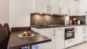 A modern kitchen with white cabinets, a dark countertop, and a dining area with a table set for two. - Beach front apartment in Binz with indoor swimming pool (Prora/Rügen)