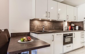 A modern kitchen with white cabinets, a dark countertop, and a dining area with a table set for two. - Beach front apartment in Binz with indoor swimming pool (Prora/Rügen)