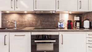A modern kitchen with white cabinets, a stainless steel range hood, a sink, a toaster, a coffee maker, and a kettle. - Beach front apartment in Binz with indoor swimming pool (Prora/Rügen)