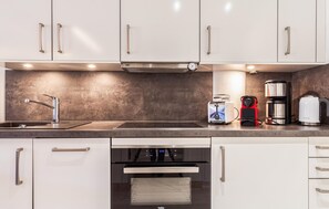 A modern kitchen with white cabinets, a stainless steel range hood, a sink, a toaster, a coffee maker, and a kettle. - Beach front apartment in Binz with indoor swimming pool (Prora/Rügen)