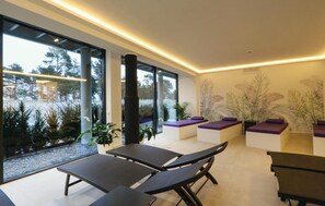 Un espacio interior moderno con ventanas amplias, una zona de estar con cojines morados y una pared con un diseño de hojas.